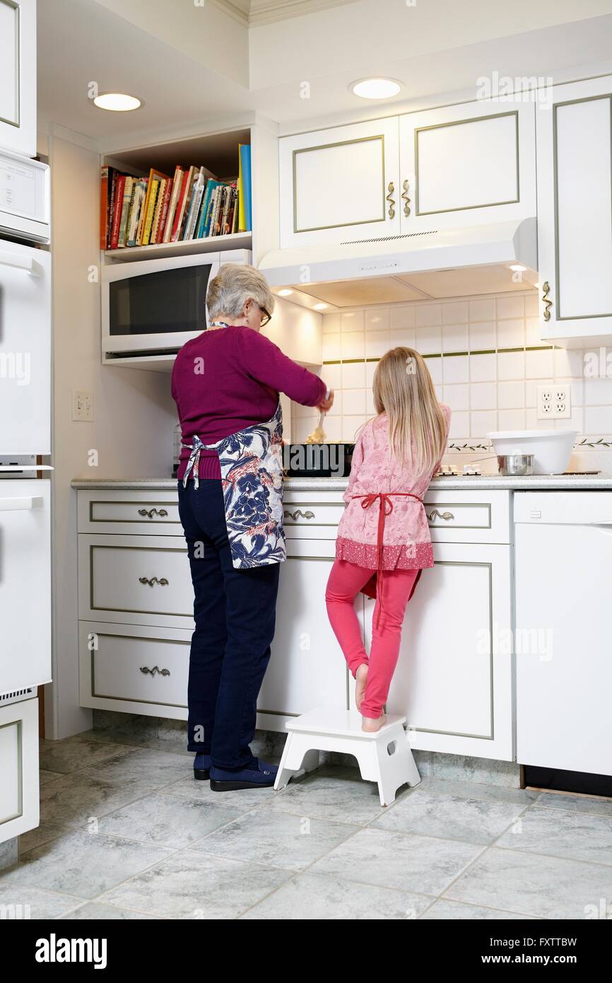 Vista posteriore di una ragazza e la nonna agitazione pentola al piano di cottura per cucina Foto Stock