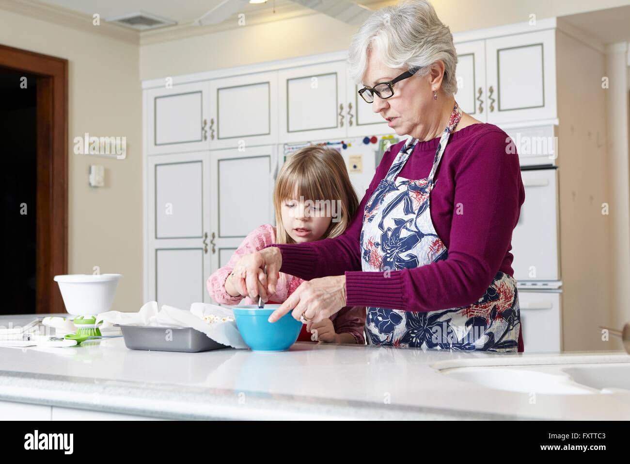 Ragazza e la nonna torta di miscelazione al banco di cucina Foto Stock
