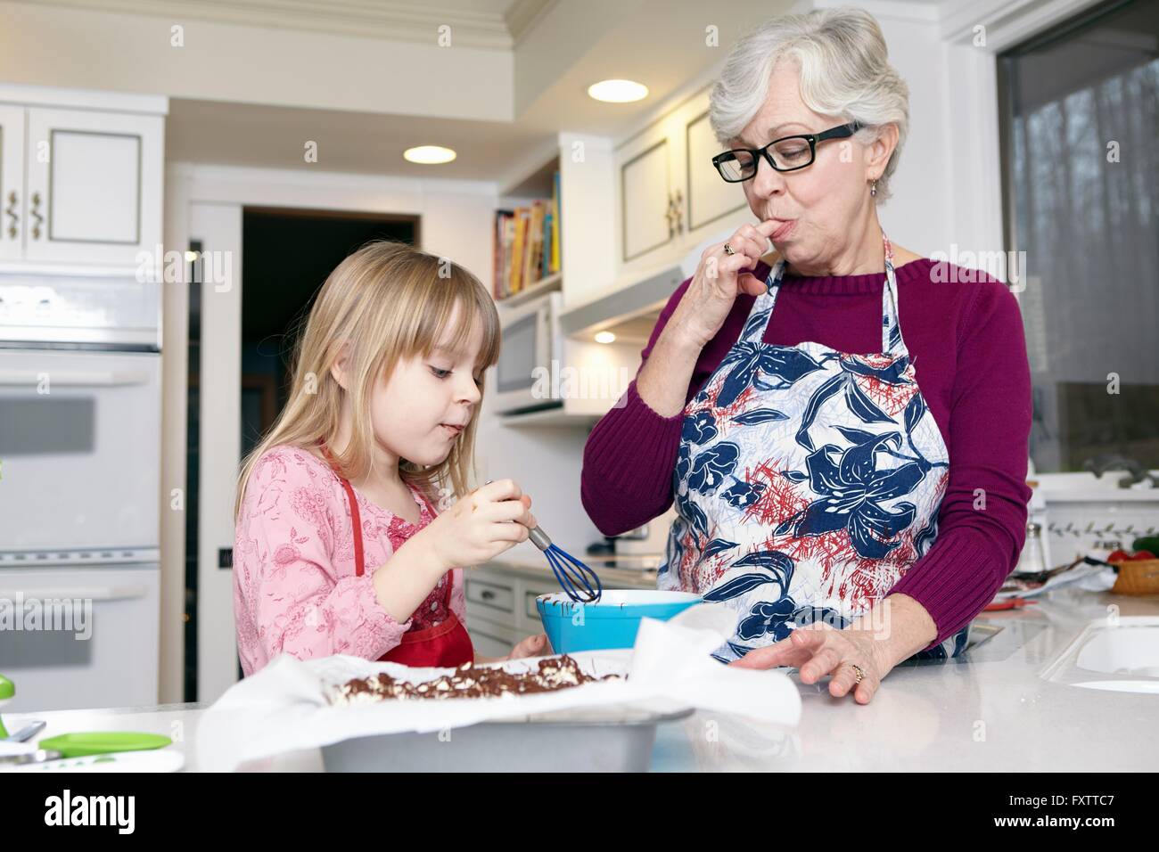Ragazza dolce di miscelazione al bancone cucina mentre la nonna leccarsi le dita Foto Stock