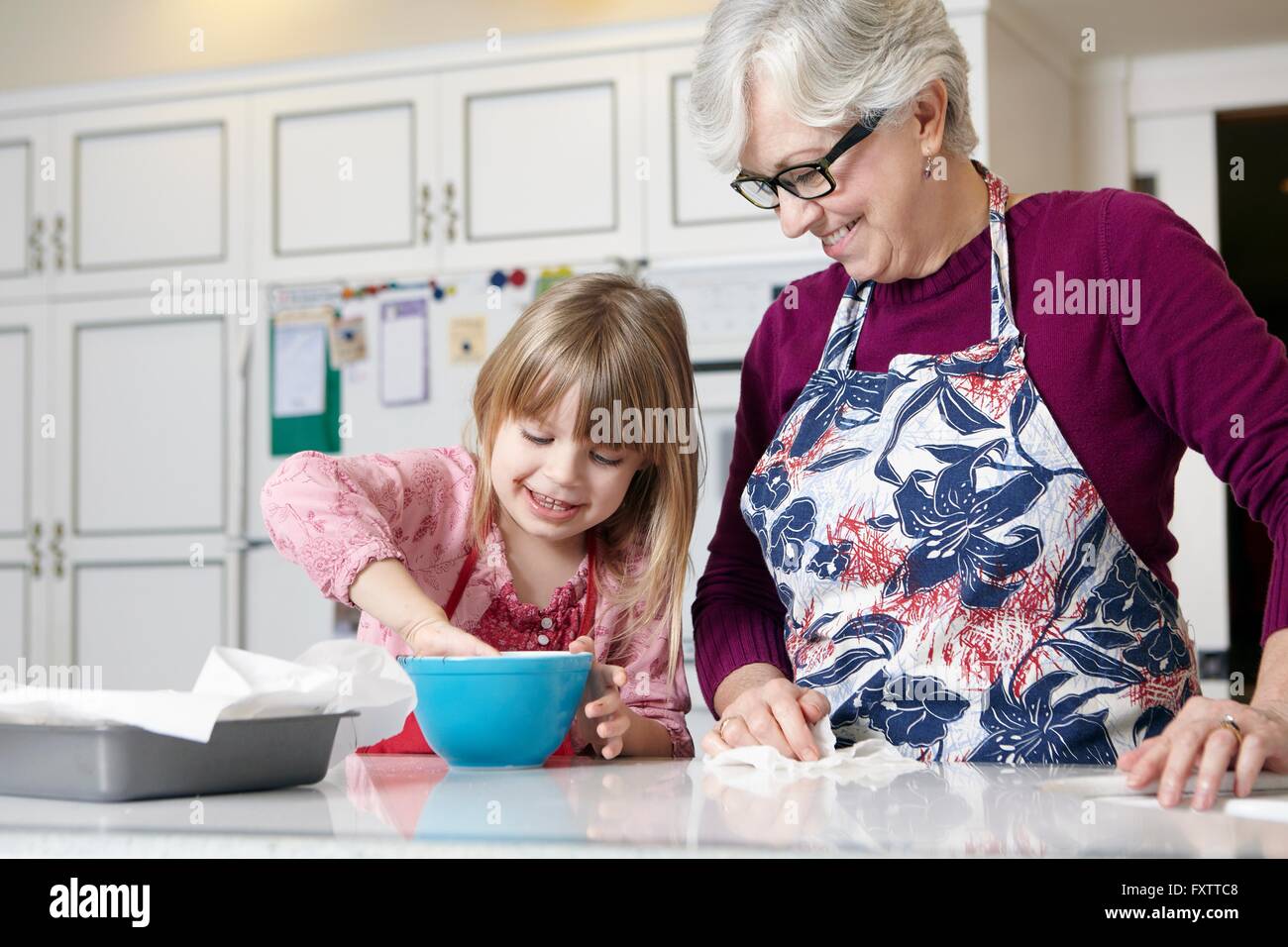 Ragazza e la nonna torta di miscelazione in un recipiente a banco di cucina Foto Stock