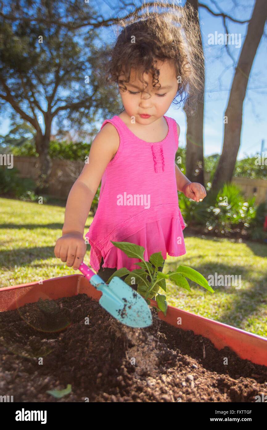 Giovane ragazza in giardino, piantare piante in vasca, tenendo cazzuola Foto Stock