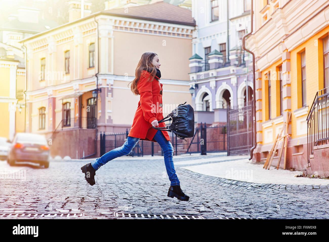 Bella giovane donna con sacco in arancione cappotto camminando sulla strada Foto Stock