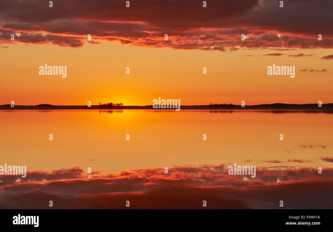 L'arancione e il rosso cielo dopo il tramonto a un lago in Finlandia. Riflessione simmetrica di nuvole nell'acqua ancora. Foto Stock