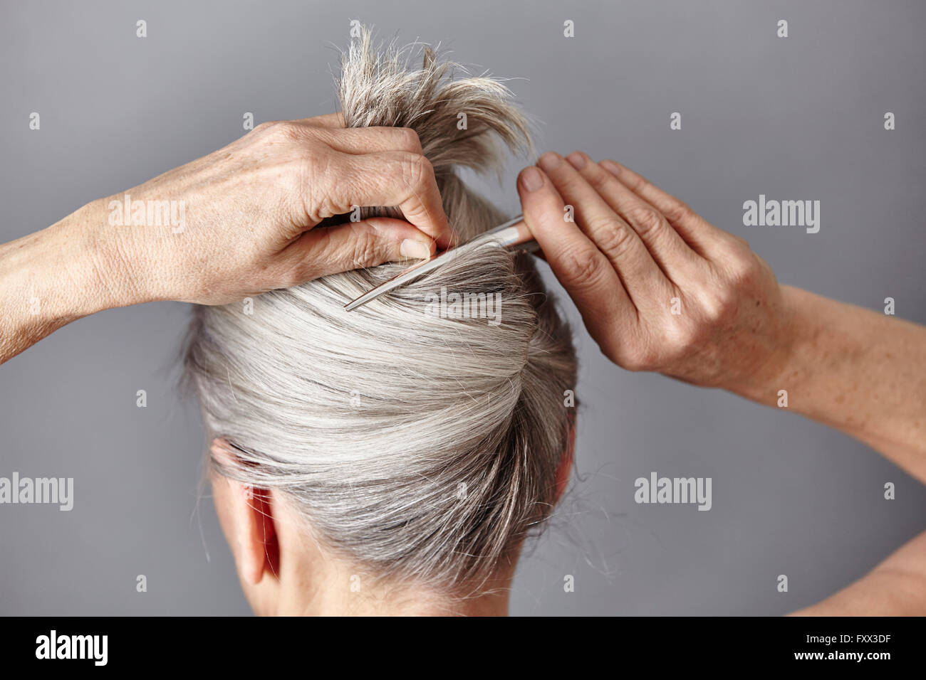 Vista posteriore della donna per lo styling dei capelli grigi in bun Foto Stock
