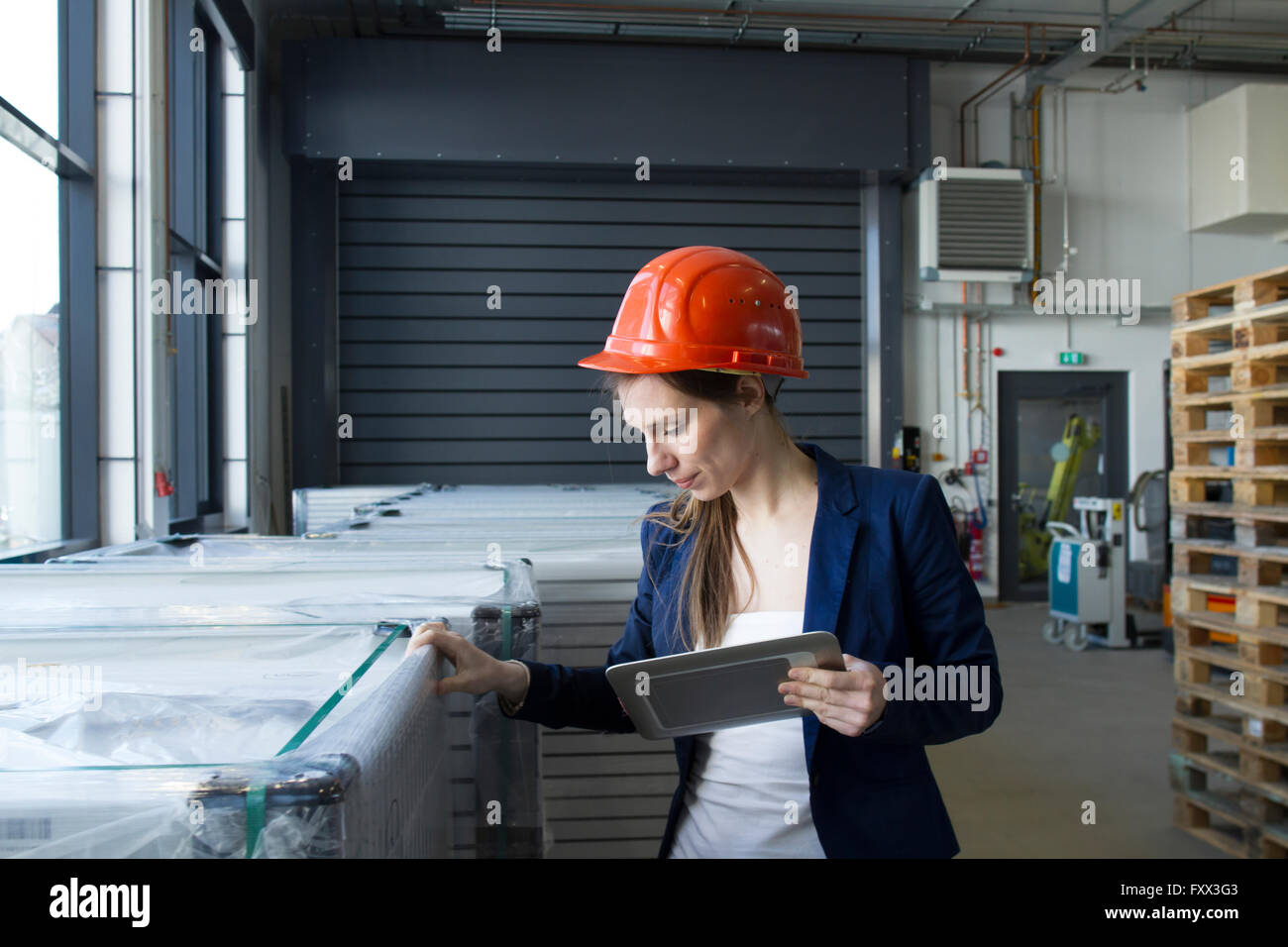 Donna in magazzino indossare elmetto in cerca azienda tavoletta digitale Controllo magazzino Foto Stock