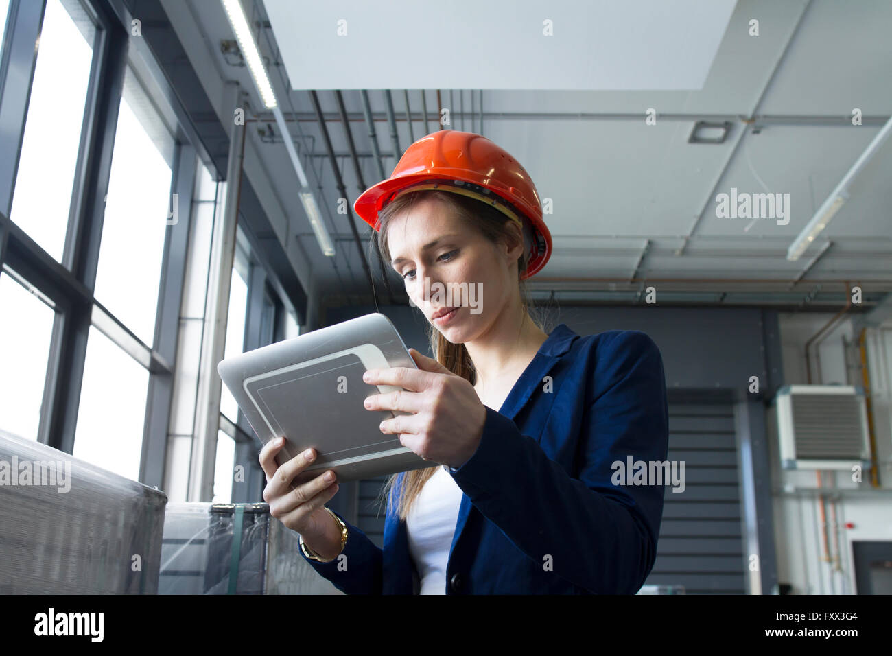 Donna in magazzino indossare elmetto guardando a tavoletta digitale Foto Stock