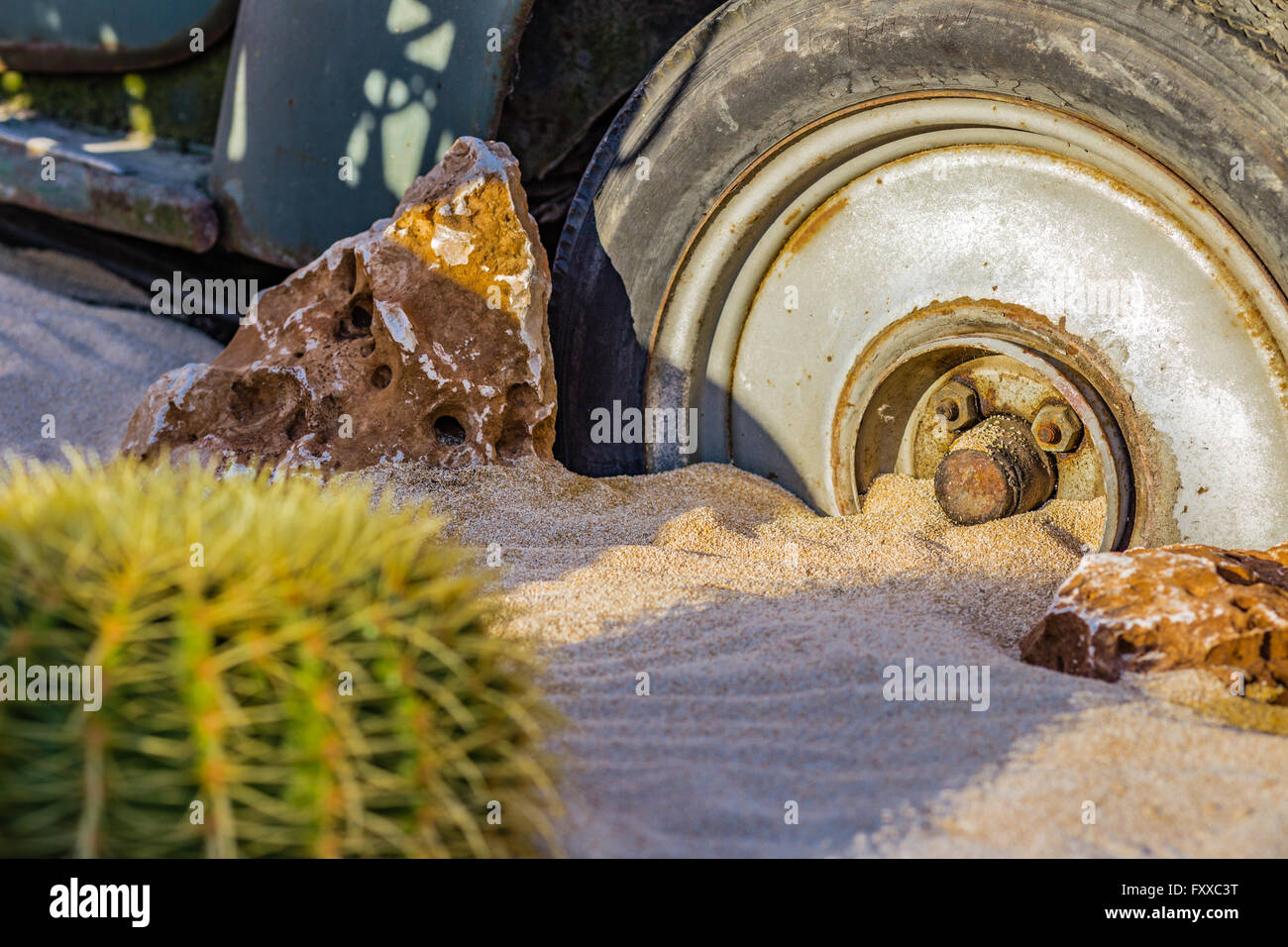 La carcassa di un vecchio arrugginito auto nel deserto di sabbia circondata da rocce e cactus Foto Stock