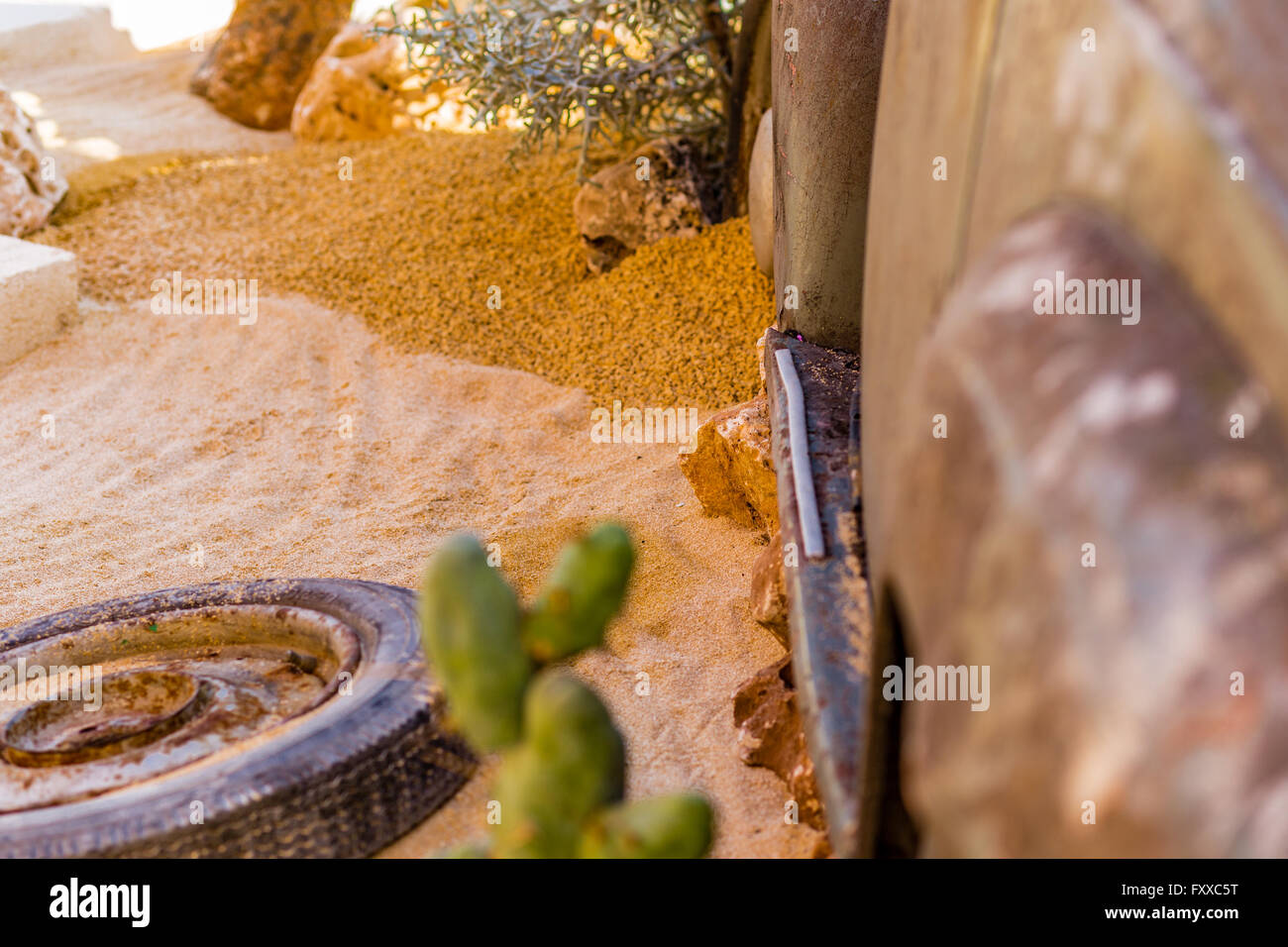 La carcassa di un vecchio arrugginito auto nel deserto di sabbia circondata da rocce e cactus Foto Stock