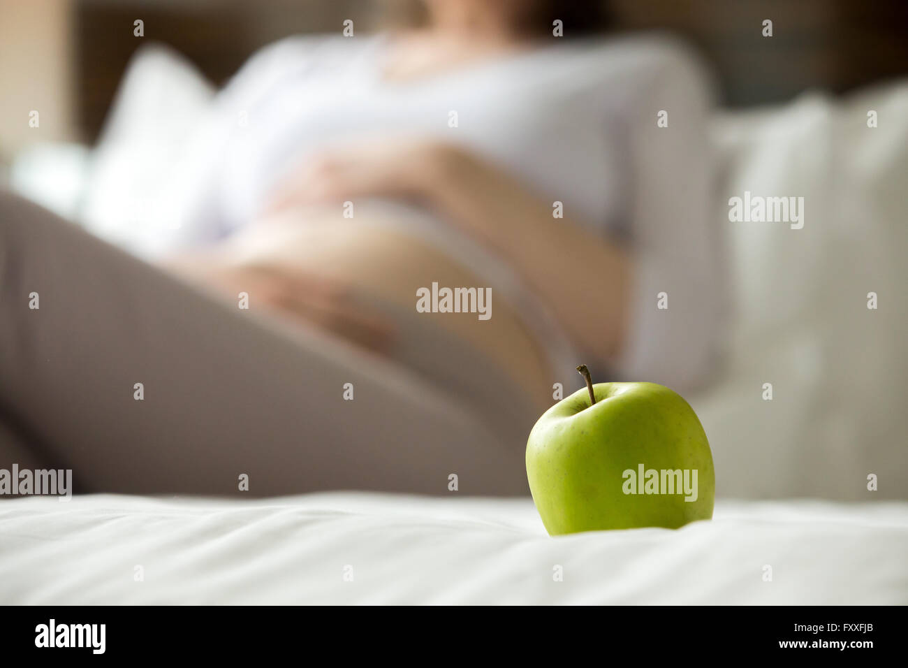 Mangiare sano concetto per donne in stato di gravidanza. Close-up di mela verde. Giovani modello incinta sullo sfondo. Futura Mamma aspetta Foto Stock
