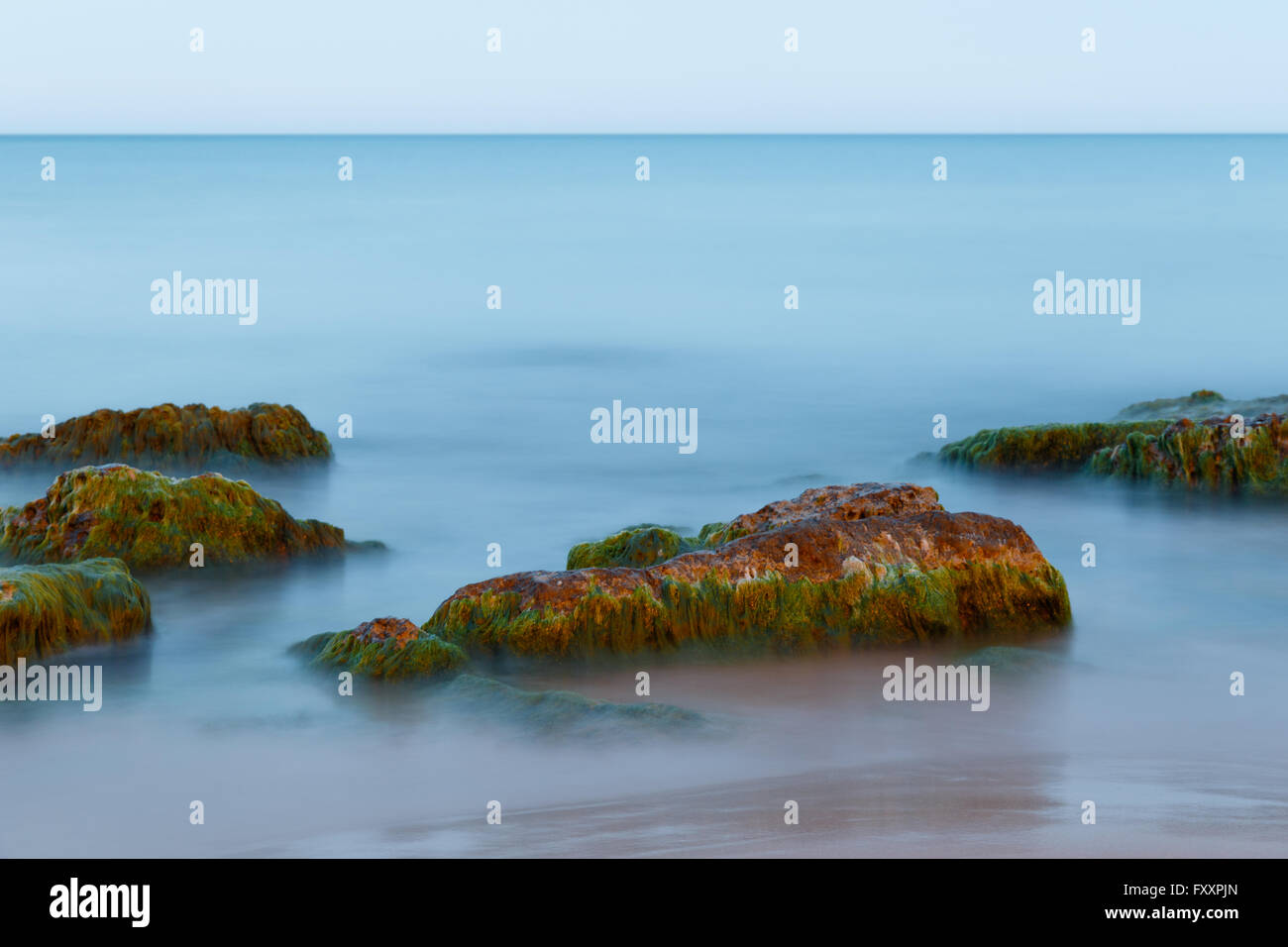 Ethereal lunga esposizione shot delle onde del mare e le rocce con verde e alghe brune a Punta Secca Beach, Italia Foto Stock