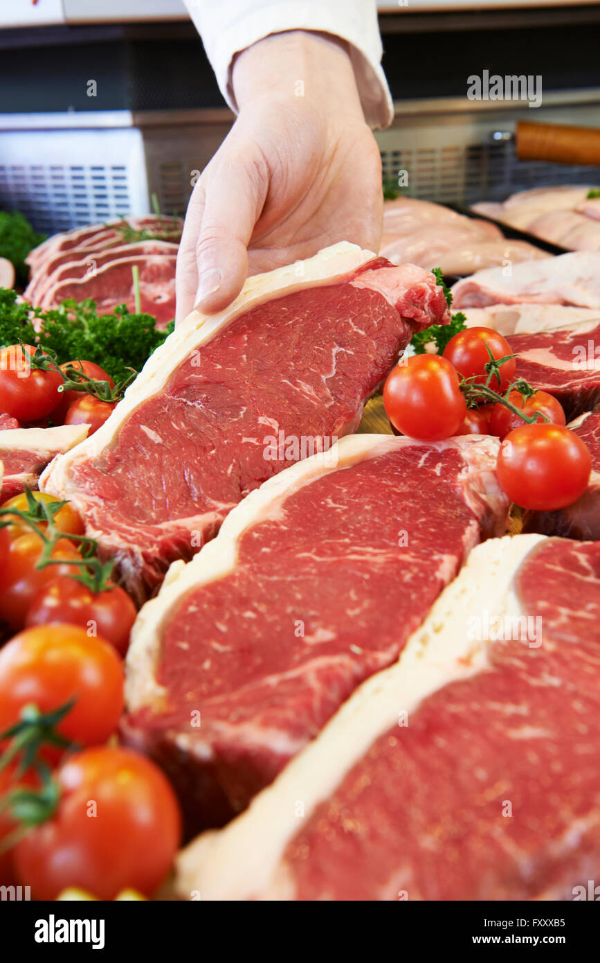 Macellaio che mostra il cliente Bistecca di controfiletto In Vetrina refrigerata Foto Stock