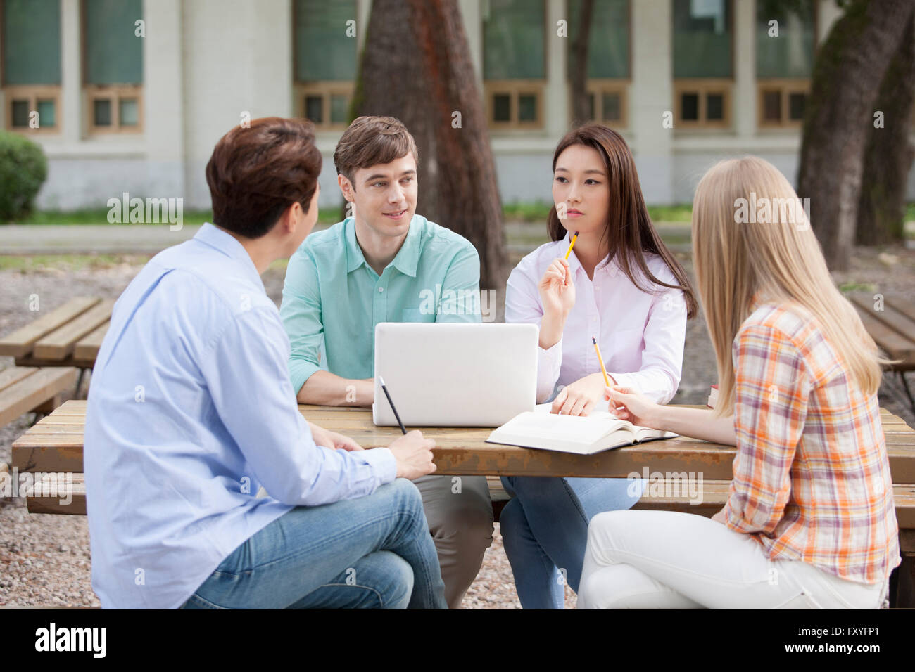 Quattro studenti del college compresi nazionali ed internazionali di studenti seduti attorno a un tavolo e avente una discussione insieme al di fuori del campus Foto Stock