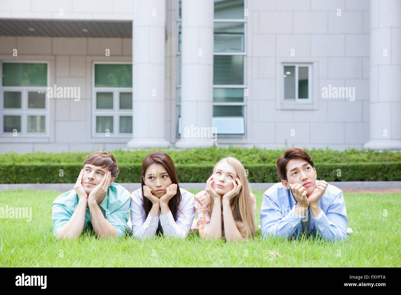 Gli studenti interni e gli studenti internazionali in college giacente sulla loro parte anteriore su erba e fissando con un sorriso al di fuori del campus Foto Stock