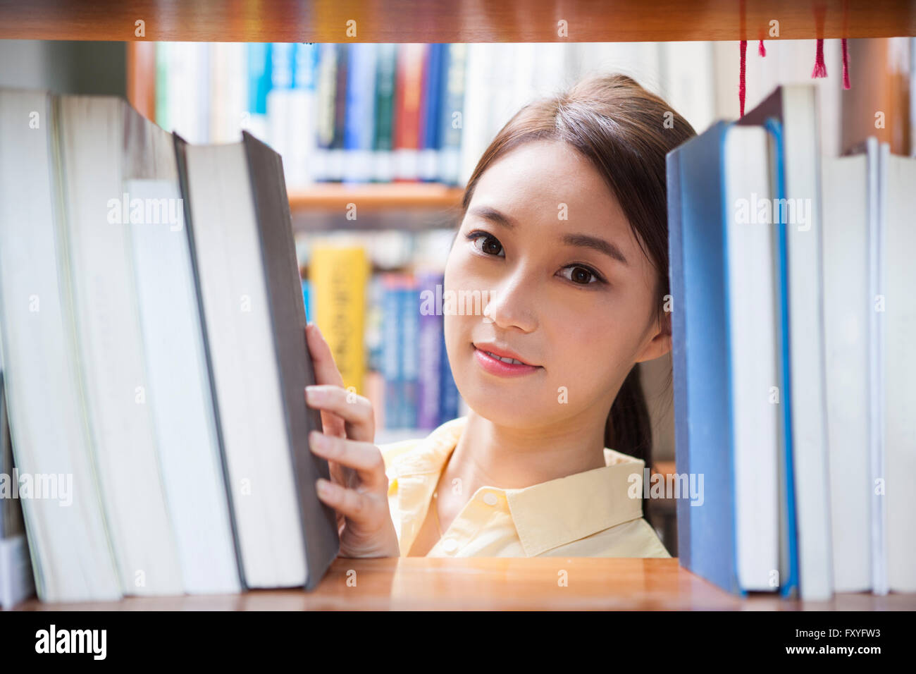 College girl cerca attraverso il libro scaffale con un sorriso presso la Biblioteca del campus Foto Stock