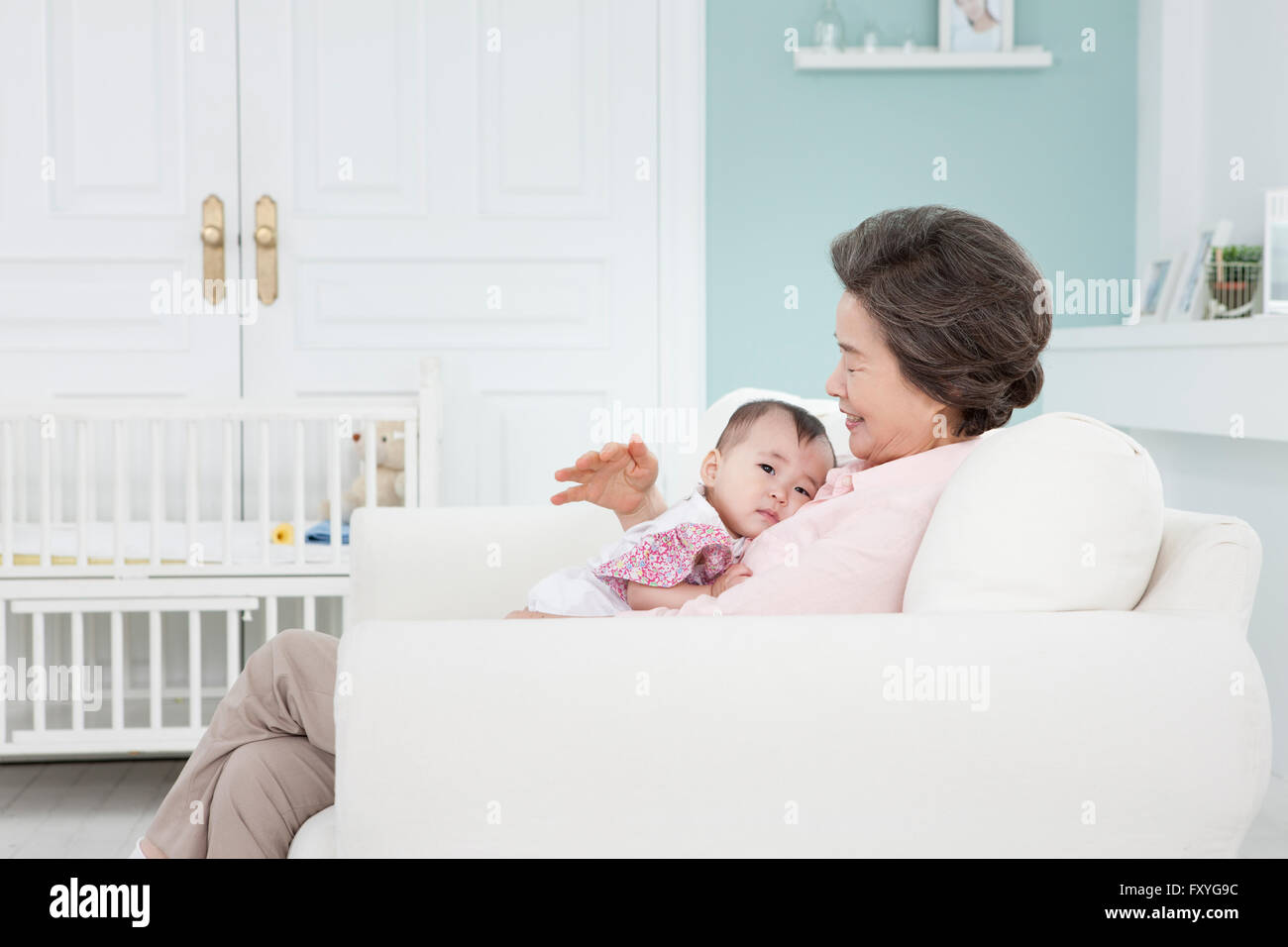 Nonna tenendo un bambino in braccio su un lettino con un sorriso Foto Stock