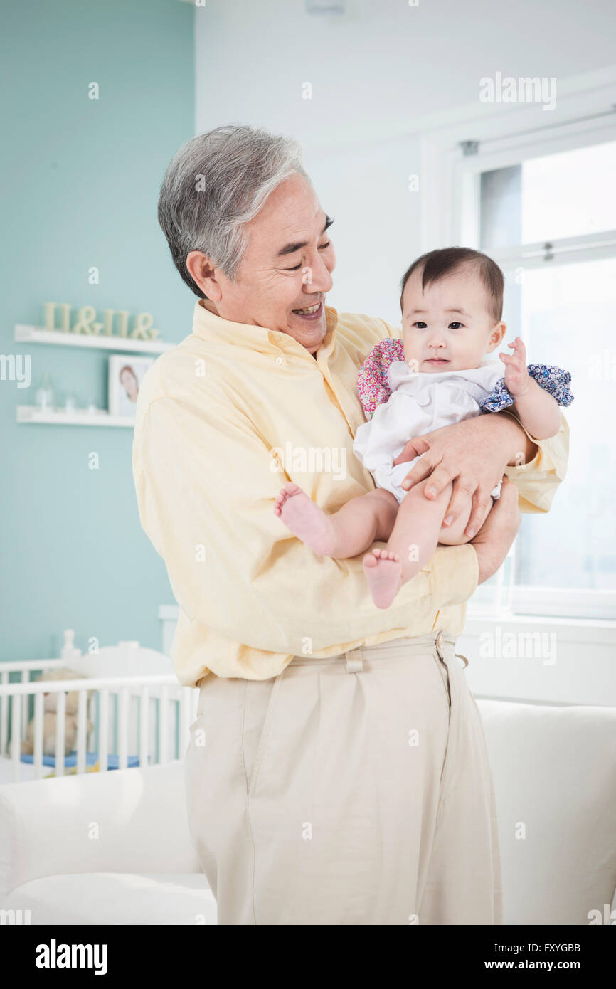 Senior uomo con un bimbo tra le braccia e per la cura del bambino con un sorriso Foto Stock