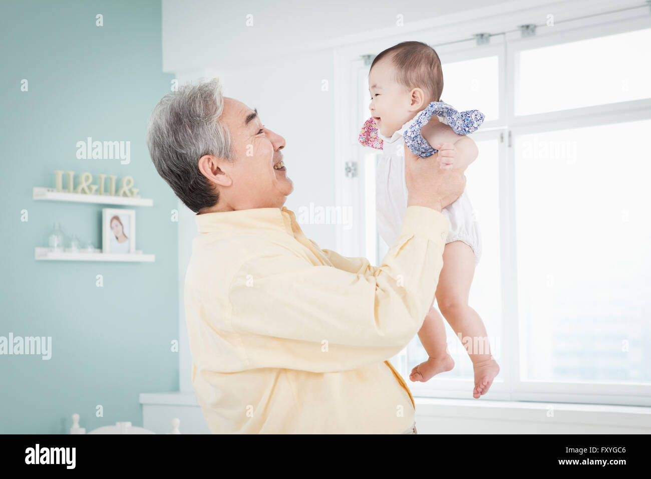 Senior man standing e tenendo un baby alta in una stanza e di prendersi cura del bambino Foto Stock