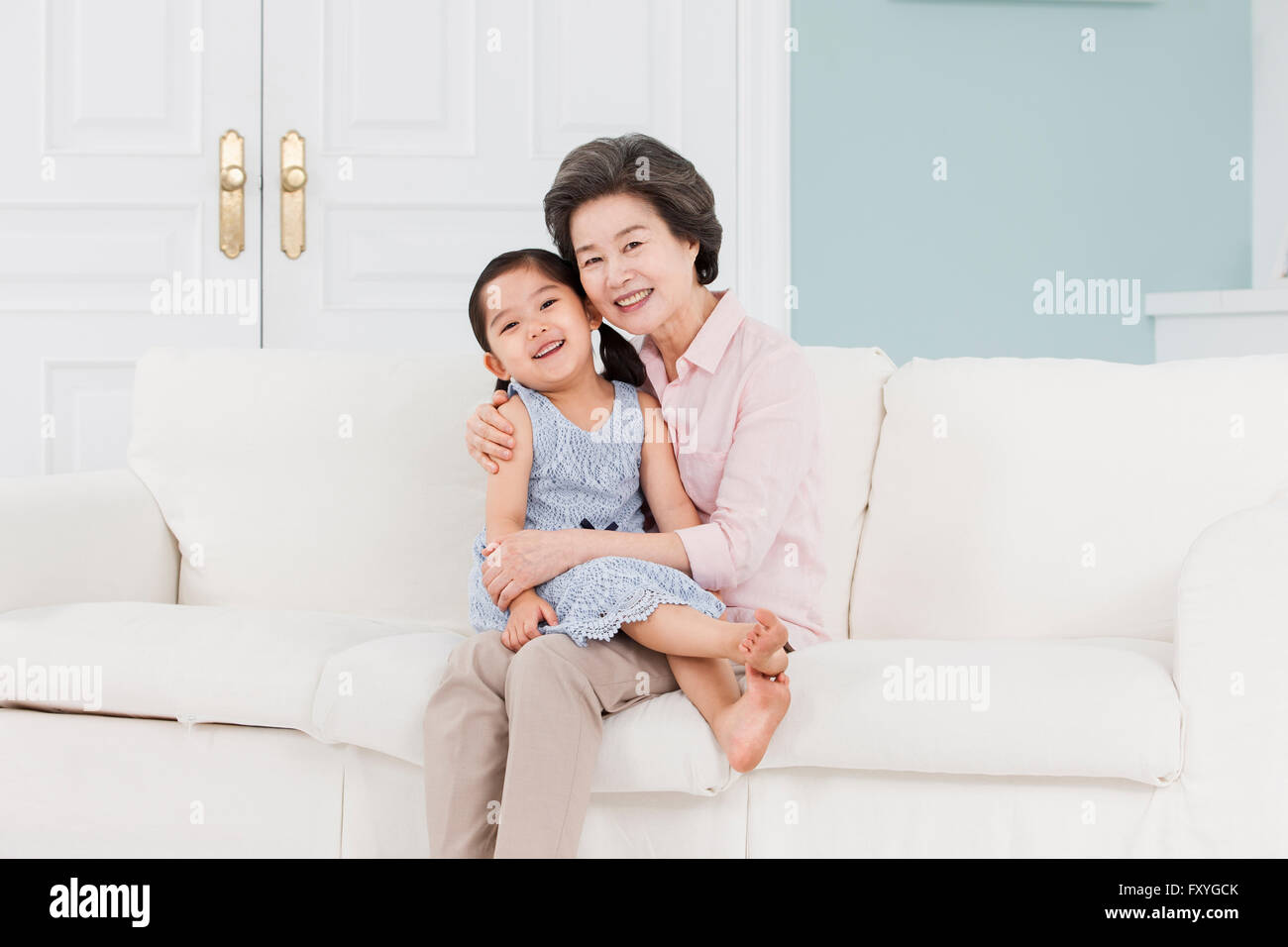 La nipote seduto sulla sua nonna il giro e la nonna seduto su un divano sia con lo sguardo in avanti con un sorriso Foto Stock