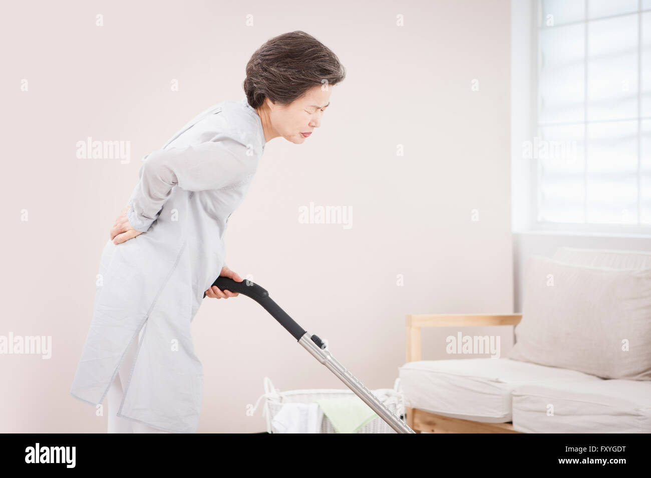 Senior sentimento Donna del dolore alla sua vita mentre aspirapolvere Foto Stock