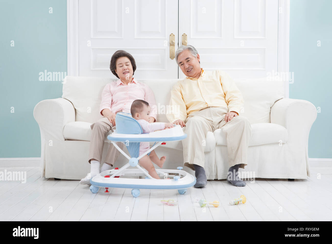Coppia senior seduto su un divano sensazione di stanchezza e di prendersi cura di un bambino su un baby walker Foto Stock