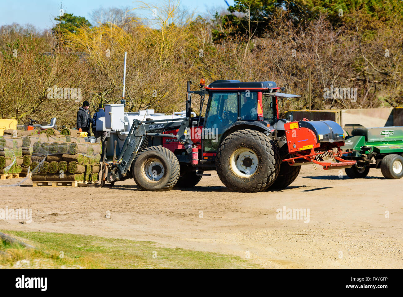 Falsterbo, Svezia - 11 Aprile 2016: Rosso Valtra 920 trattore è carico di un pallet pieno di rotoli di erba vicino ad un campo da golf. Foto Stock
