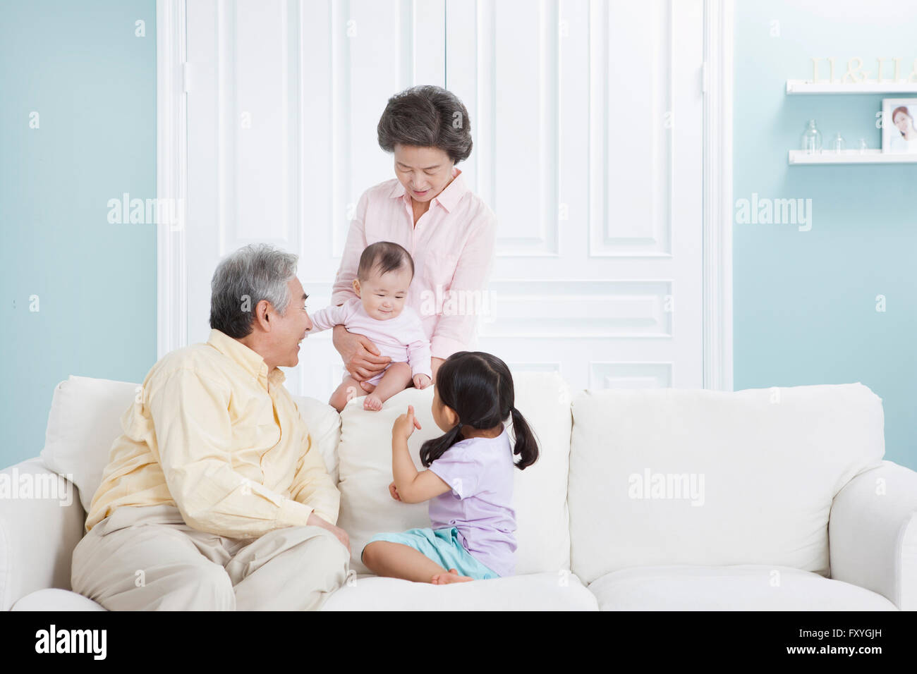 Nonna tenendo un bambino dietro un lettino ed un nonno con il nipote seduto su un lettino e guardando il bambino con un sorriso Foto Stock