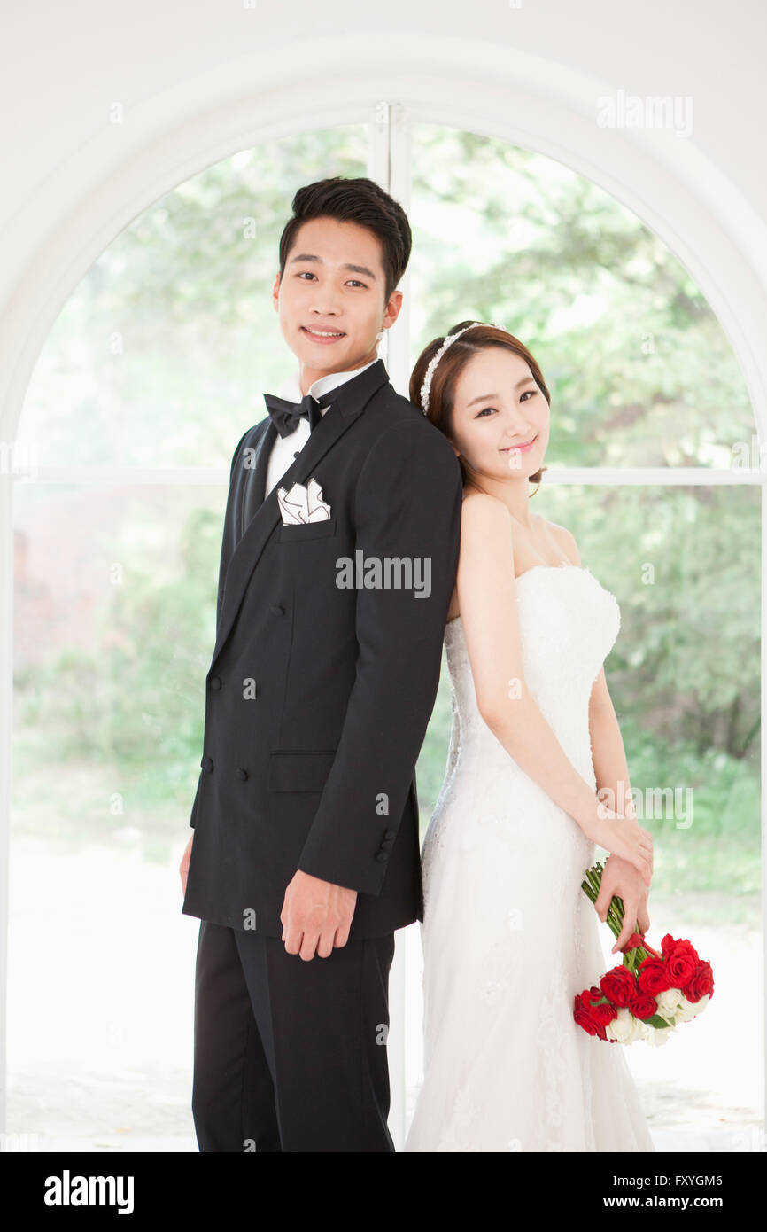 Sposa con un bouquet mettendo schiena a schiena con lo sposo entrambi con lo sguardo in avanti con un sorriso Foto Stock