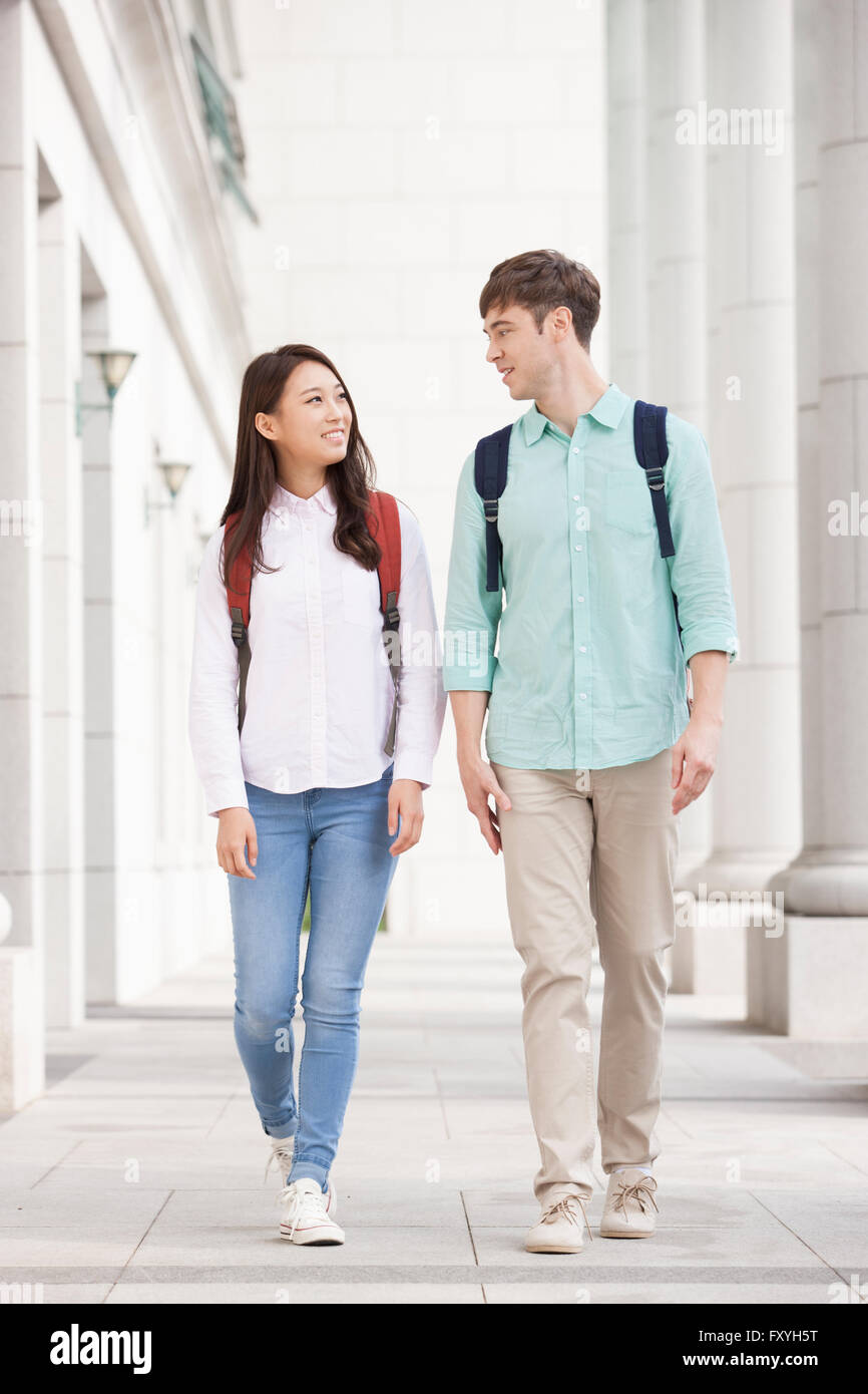 College girl e un maschio international student camminando sul campus insieme e guardando a vicenda con un sorriso Foto Stock