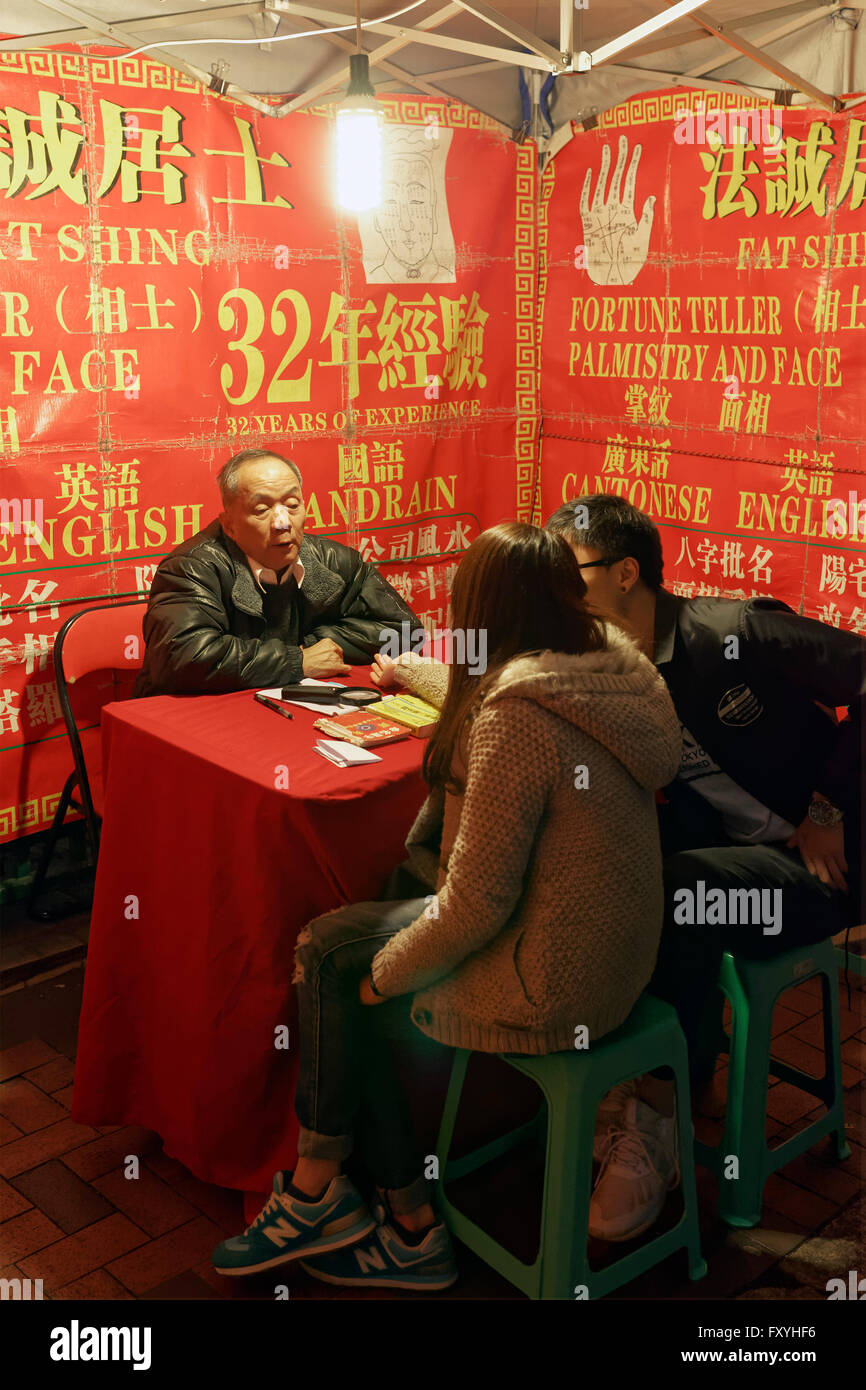 Indovini cinesi in una tenda illuminata, la lettura di una giovane donna di Palm, il Mercato Notturno di Temple Street, Yau Ma Tei, Kowloon, Hong Kong Foto Stock