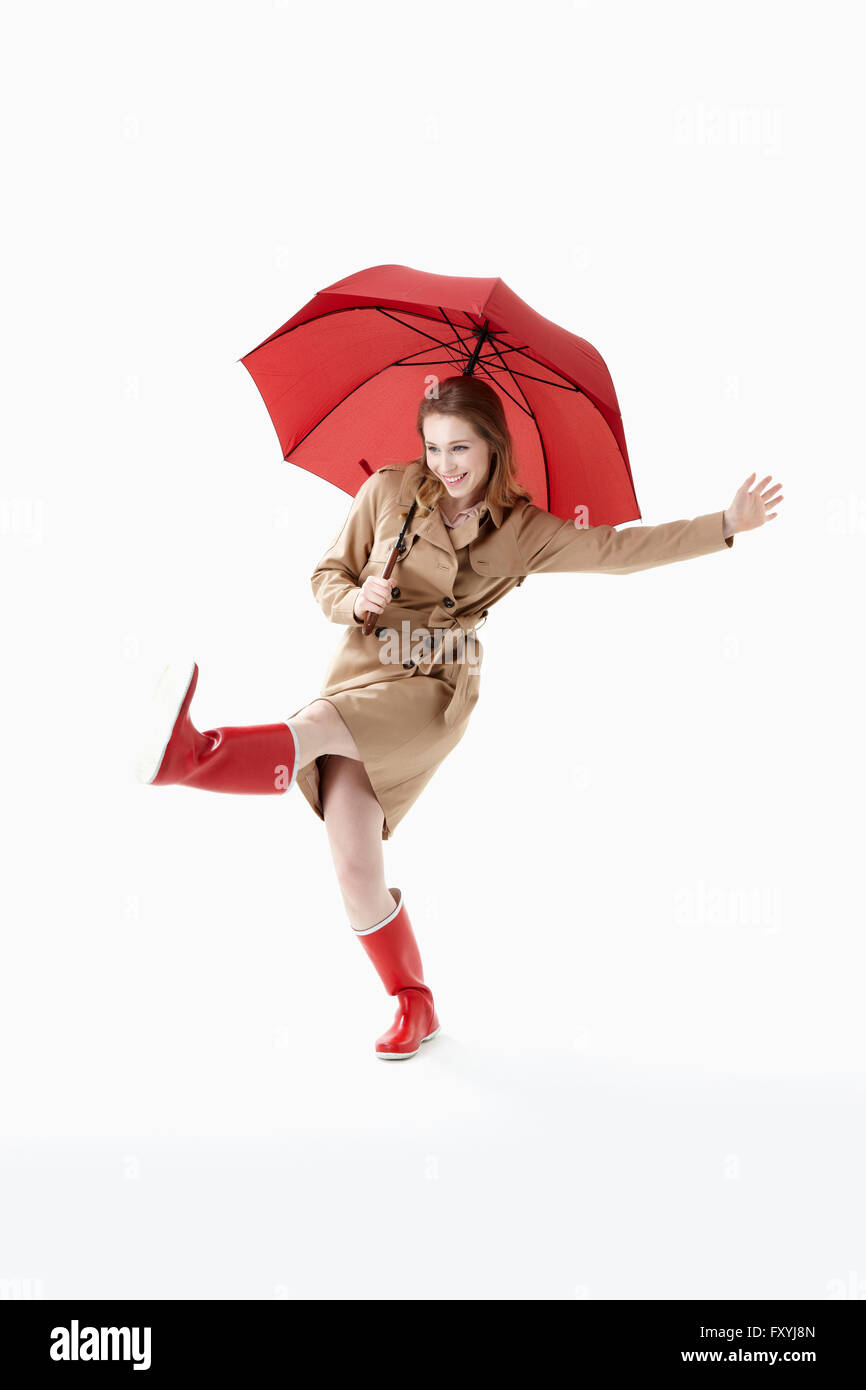 La donna a trench coat tenendo un ombrello rosso con un gesto di calci Foto Stock