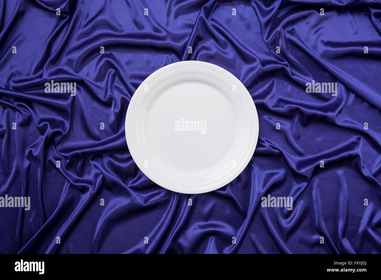 Elevato angolo di una piastra bianca su blu panno di seta Foto Stock