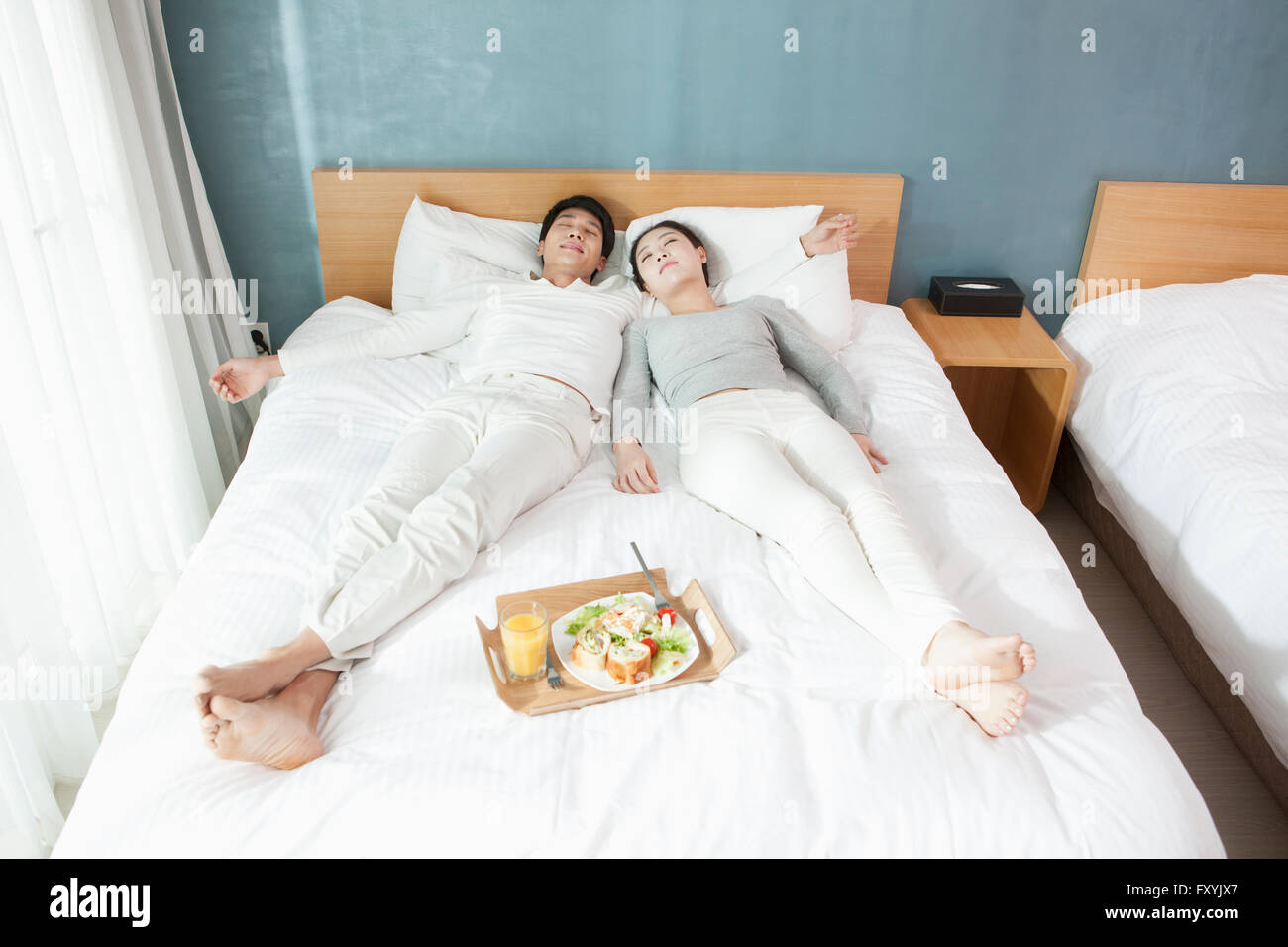 Elevato angolo di giovane sdraiato sul letto con vassoio di prima colazione in camera resort Foto Stock