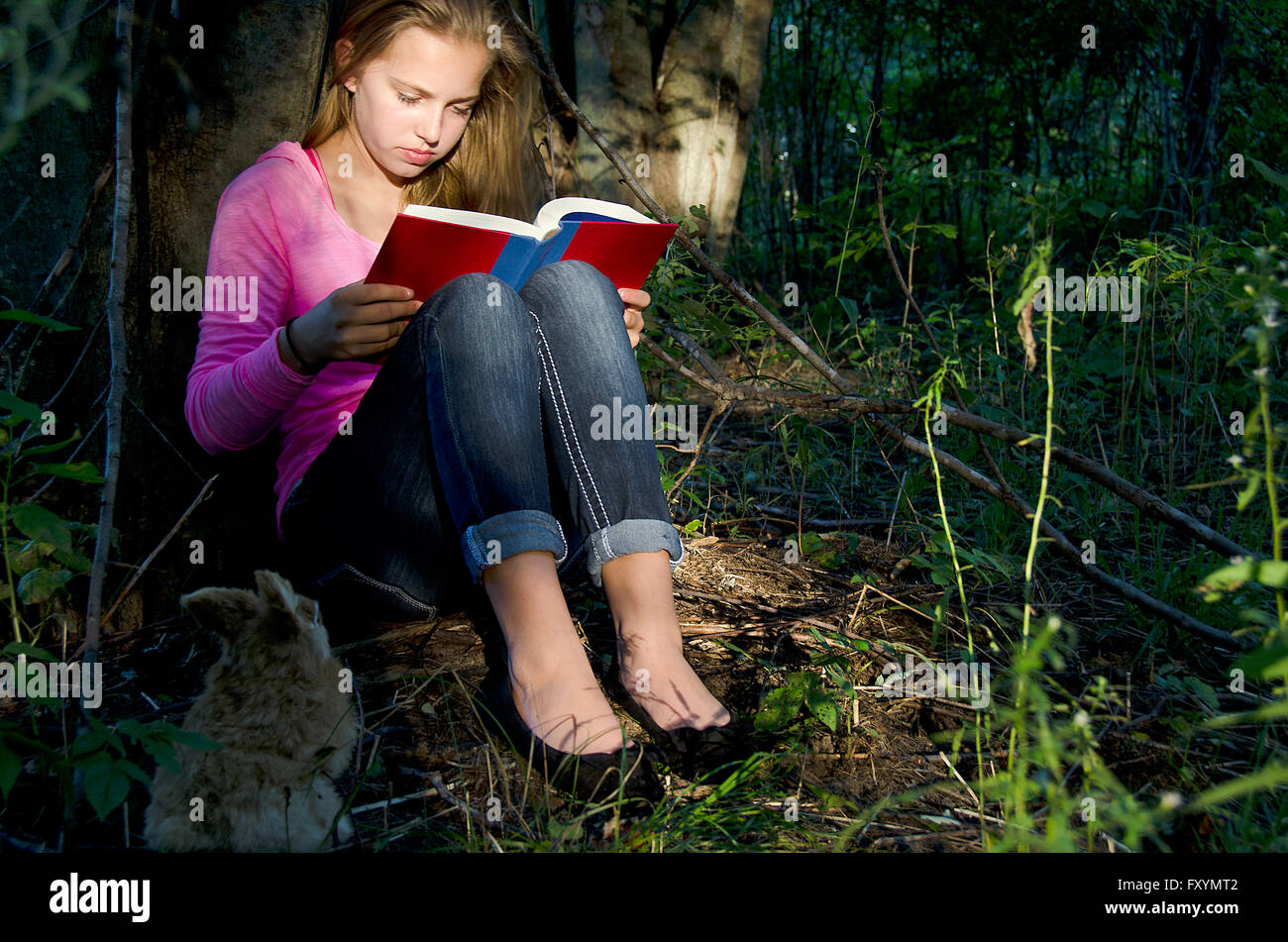 Ragazza giovane leggendo un libro nella luce del sole nella foresta con coniglio. Foto Stock