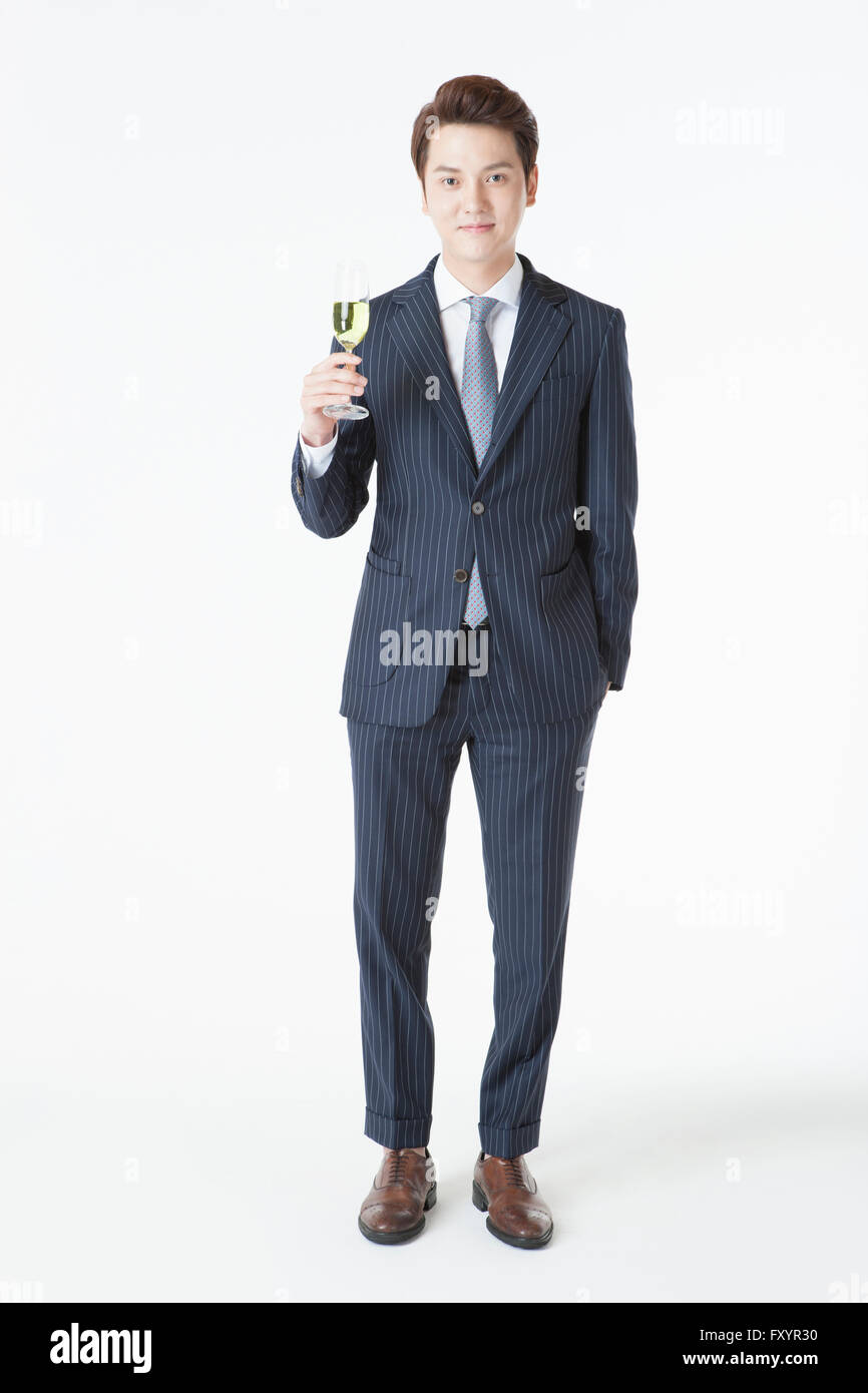Giovane uomo sorridente in tuta in piedi con un bicchiere di champagne con lo sguardo sul lato anteriore Foto Stock