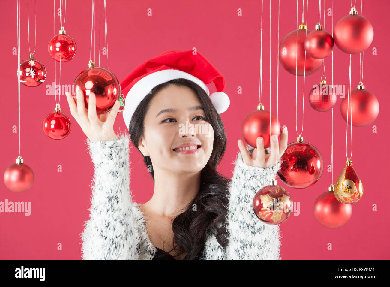 Ritratto di giovane donna sorridente indossando santa hat toccando le palle di Natale cercando Foto Stock