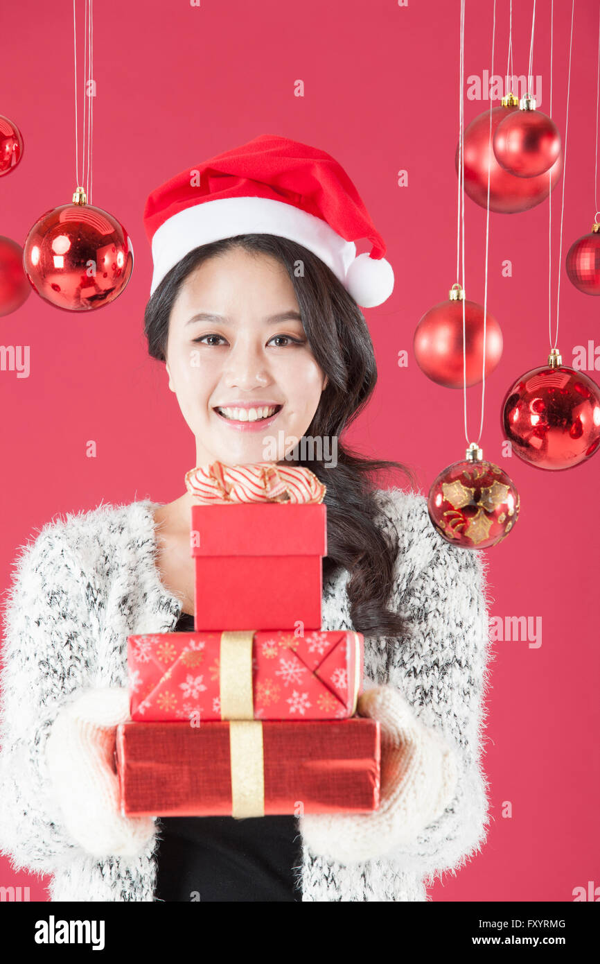 Ritratto di giovane donna sorridente indossando santa hat holding impilati confezioni regalo staring al fronte con le palle di Natale Foto Stock