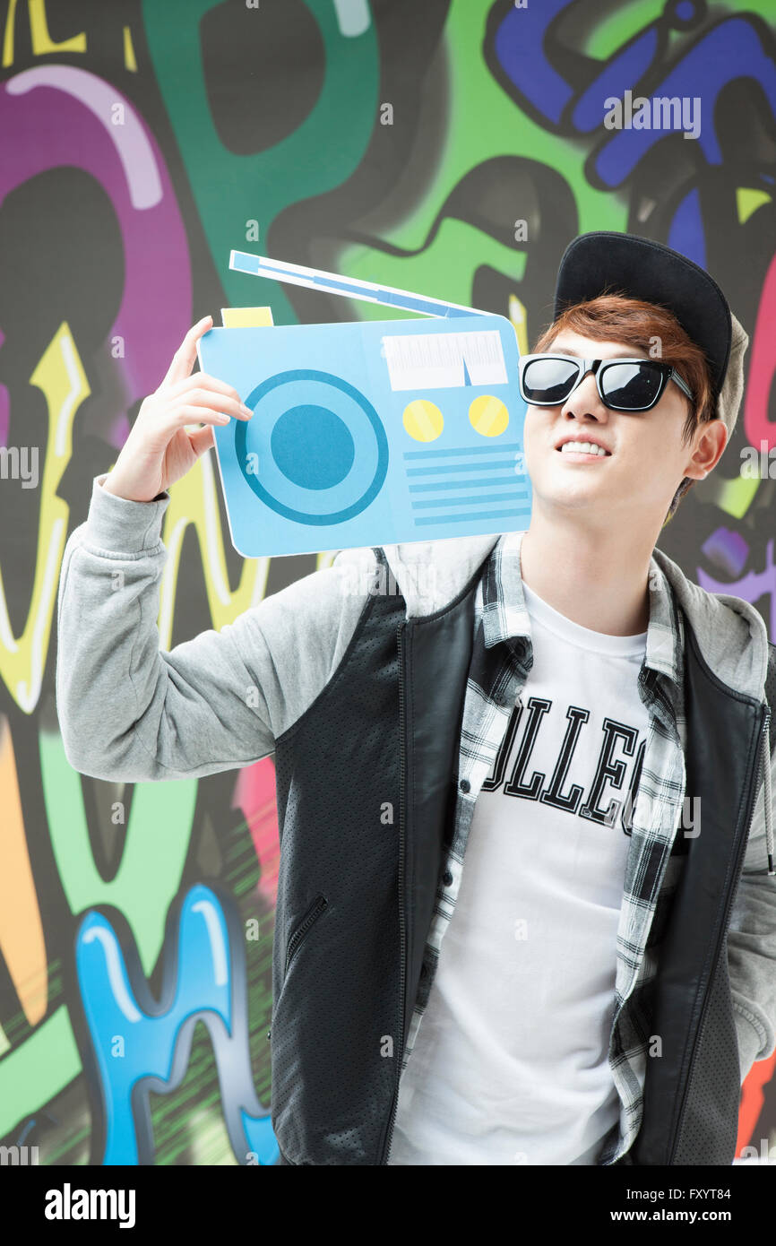 Ritratto di giovane uomo sorridente in hip-hop con stile con una radio cercando contro arte dei graffiti Foto Stock