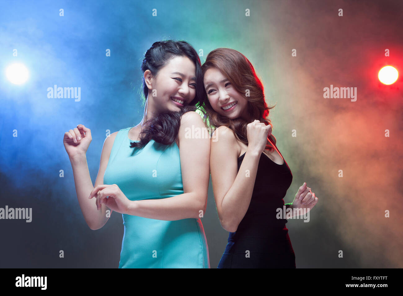 Ritratto di due giovani donne sorridenti dancing back to back faccia a faccia in illuminazioni Foto Stock