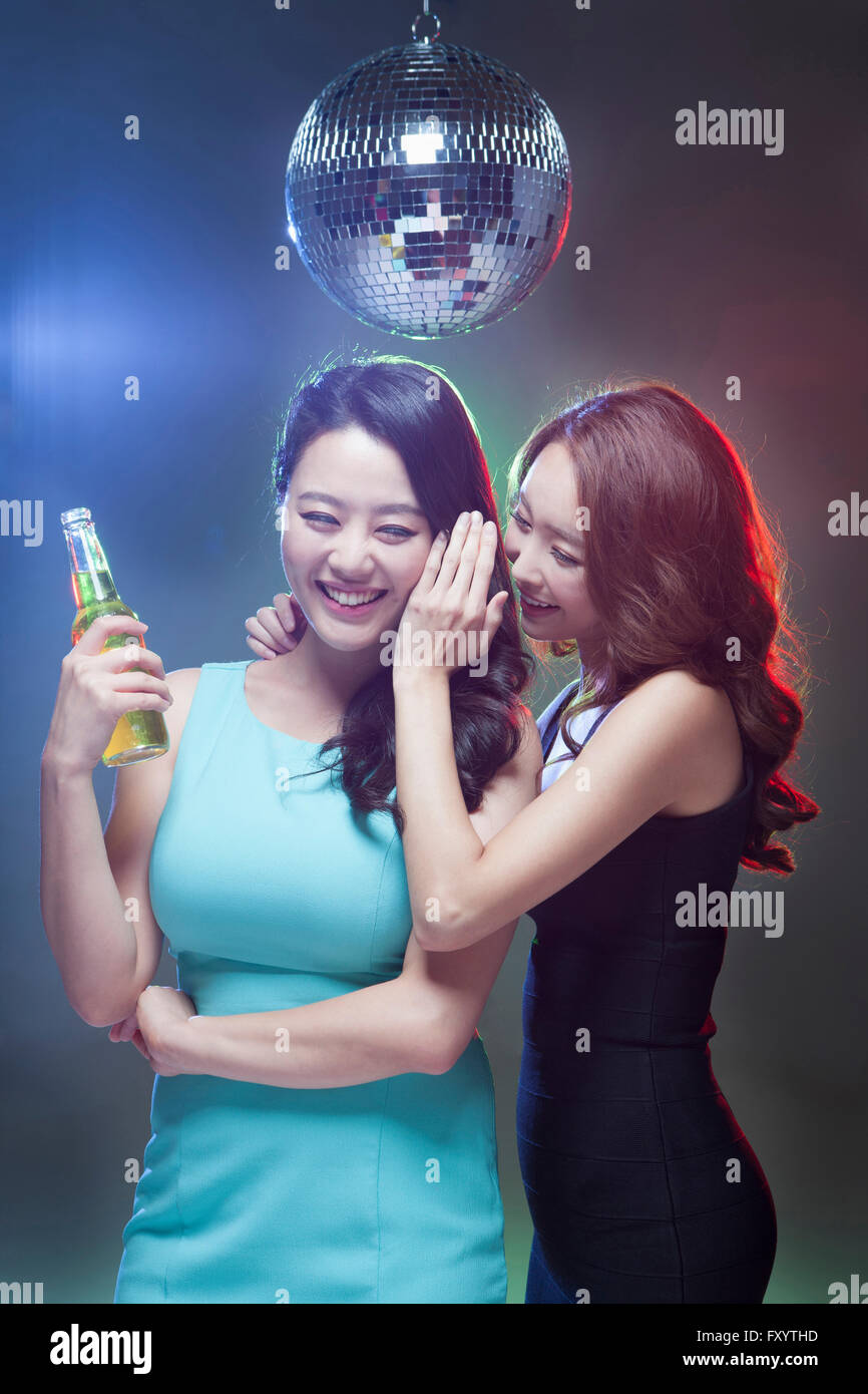 Due giovani donne sorridenti parlando in un sussurro con bottiglia di birra sotto una sfera dello specchio Foto Stock