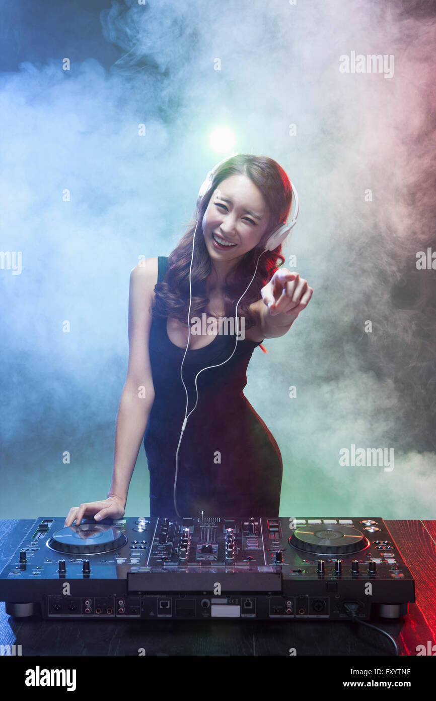 Giovane donna sorridente DJ riproduzione di musica rivolto alla parte anteriore, fissando sulla parte anteriore Foto Stock