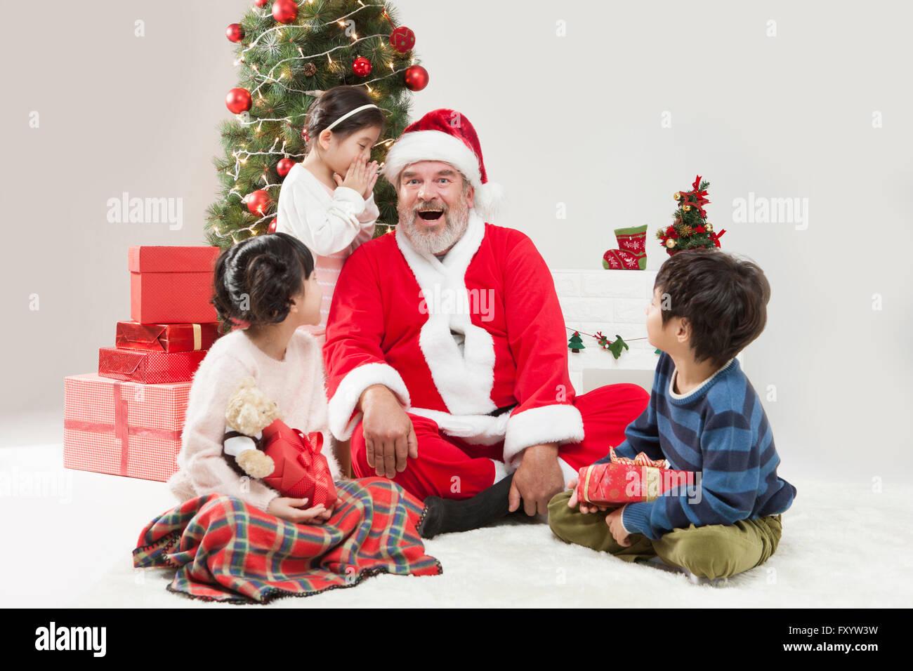 Ragazza sorridente e Santa Claus parlando in un sussurro, un ragazzo e una ragazza a guardarli a Natale Foto Stock