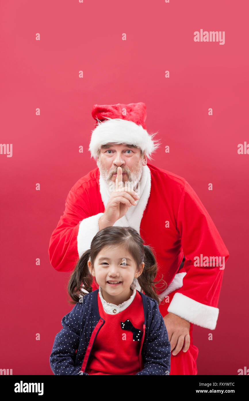 Ritratto di ragazza sorridente e Santa mettere il dito sulle sue labbra dietro di lei lo sguardo sul lato anteriore Foto Stock