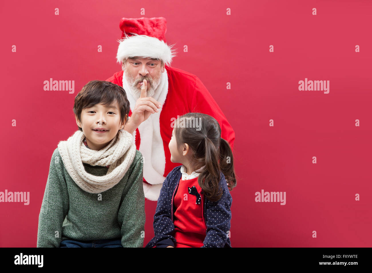 Ritratto di ragazzo sorridente fissando anteriore, sorridente Santa mettendo la sua mano sulle sue labbra e sorridente ragazza faccia a faccia Foto Stock