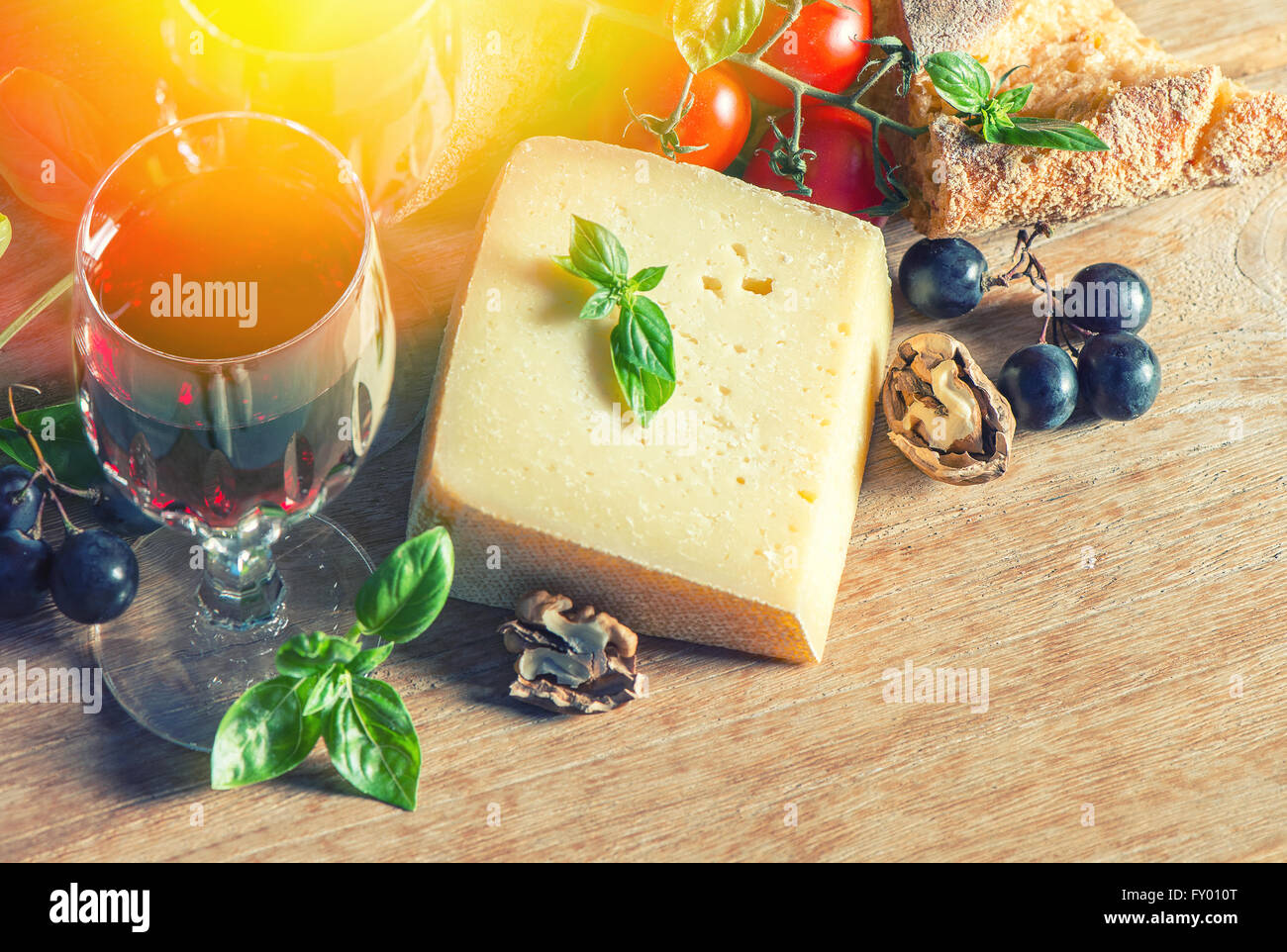 Formaggio con vino rosso, noci, pomodori e le foglie di basilico e uva. Sfondo di cibo. In stile vintage tonica immagine di luce leacks Foto Stock