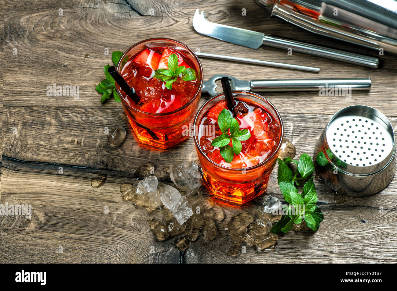 Red cocktail con Fragola, foglie di menta, ghiaccio. Fare Drink bar accessori sul tavolo di legno Foto Stock