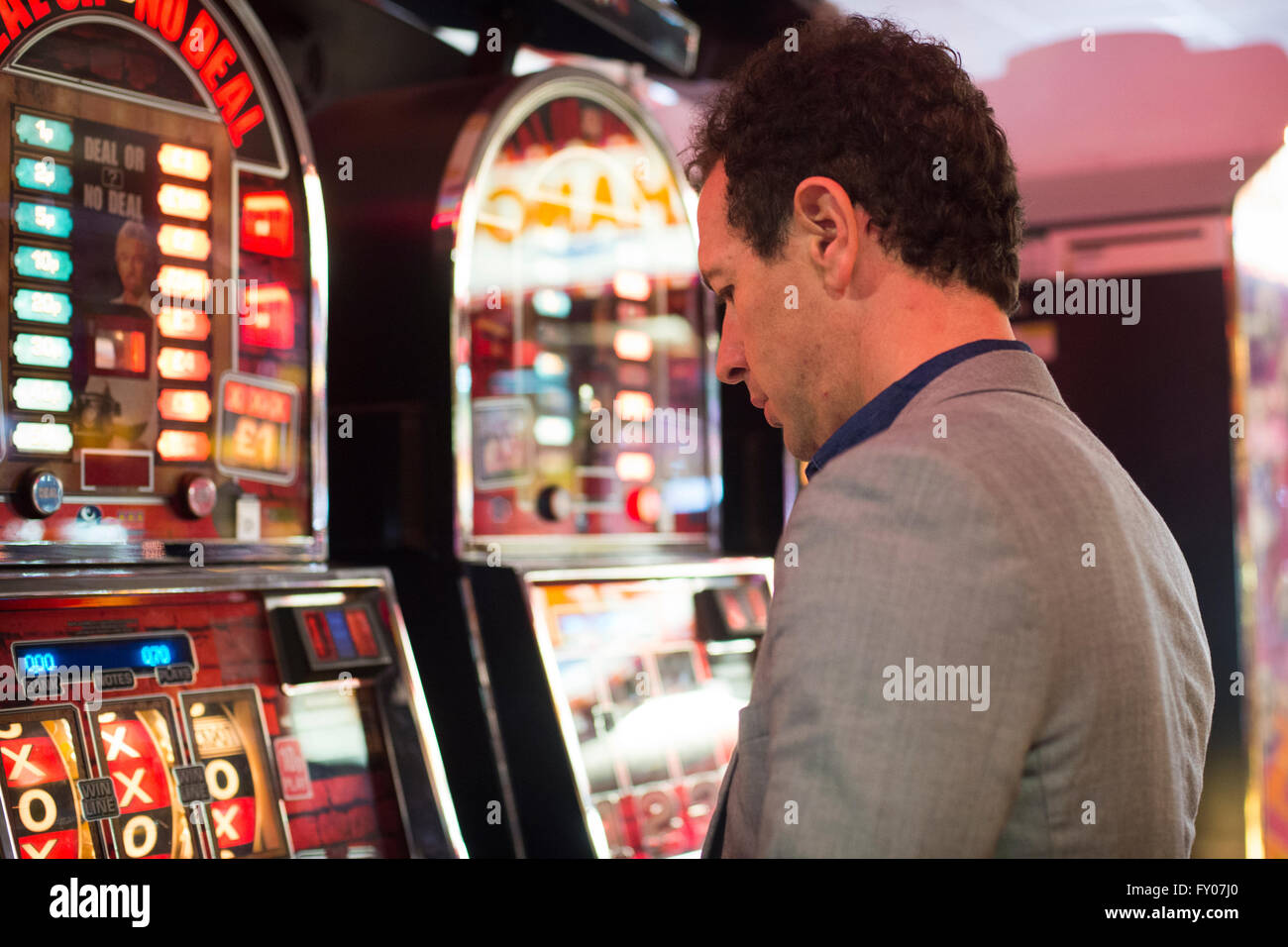 L'uomo il gioco d'azzardo nel casino con macchine di frutta perdendo denaro Foto Stock