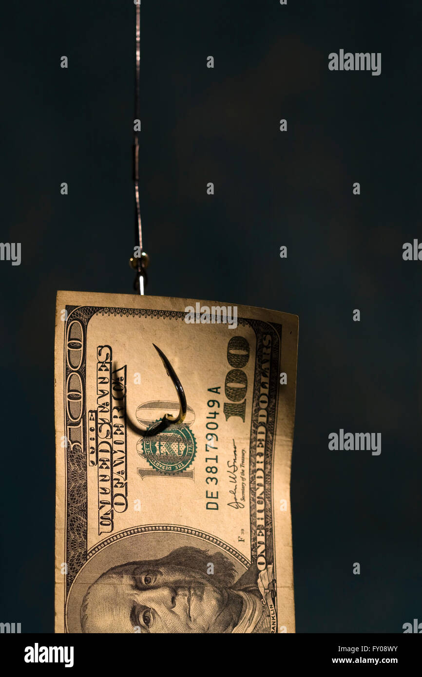 La metà di un $100 bill appeso su un amo da pesca con luce sfondo blu Foto Stock
