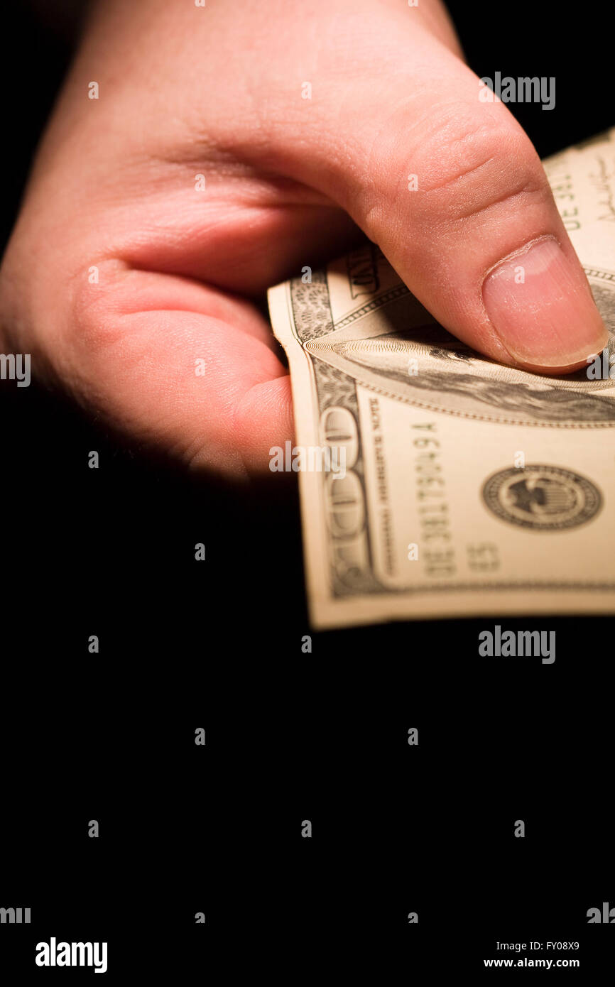 Un uomo della mano destra emergendo dalle ombre tenendo fuori un $100 bill Foto Stock