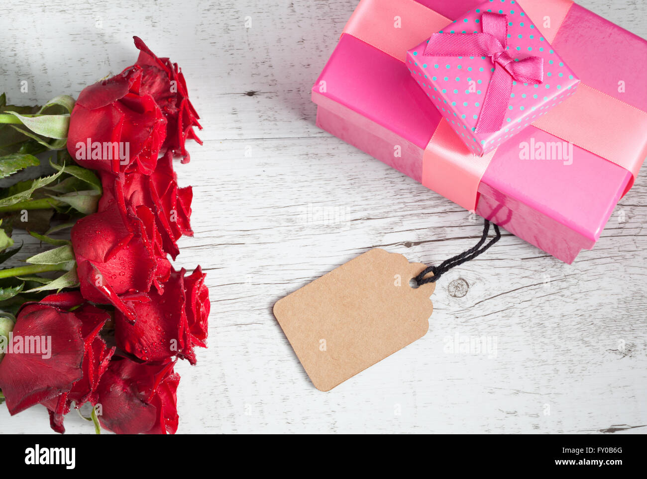 Regalo romantico concetto con rose rosse, confezioni regalo, e tag vuoto su bianco tavola in legno rustico. Vista da sopra con copia spazio. Foto Stock