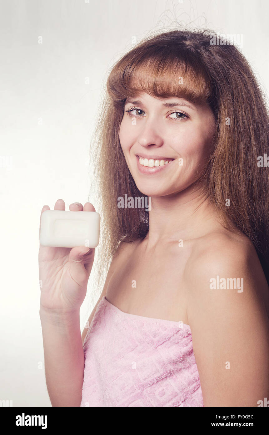 La donna in un asciugamano detiene il sapone in mano e sorrisi con denti. Foto Stock